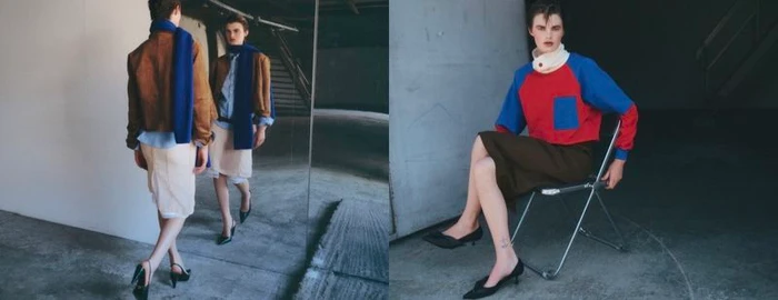Model wearing a color-blocked top and dark skirt seated on a folding chair in an industrial space
