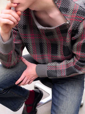 Close-up of a model wearing a grey plaid sweater with a diagonal zipper and denim jeans