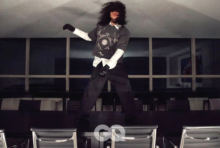 Model Sanggun Lee with long dark hair covering eyes, standing on a large conference table in GQ Korea Night Shift project