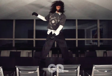 Model Sanggun Lee with long dark hair covering eyes, standing on a large conference table in GQ Korea Night Shift project