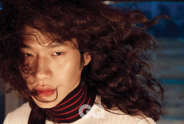 Close-up portrait of model Sanggun Lee with long dark curly hair and a striped turtleneck for GQ Korea