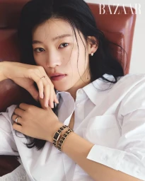 Model Sol Jeong wearing a white shirt and chain-strap watch leaning on a brown leather armchair for Harper's Bazaar Korea.