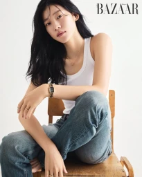 Model wearing a white tank top and blue jeans sitting on a wooden chair against a plain white background