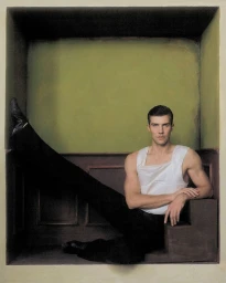Dancer Roberto Bolle wearing a white sleeveless top and black trousers seated inside a boxed room set
