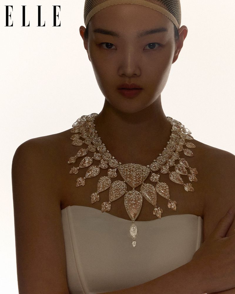 Model wearing an elaborate diamond necklace and white strapless top against a bright backlit background with ELLE logo
