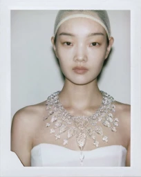 Model wearing a diamond necklace and a white strapless top with a hair net against a light background.