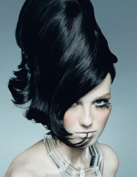 Model with elaborate voluminous black updo hairstyle and clear geometric choker necklace against grey background