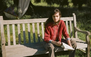 Model Ster Vieira seated on a wooden park bench wearing a red patterned top for The Gentlewoman project Here