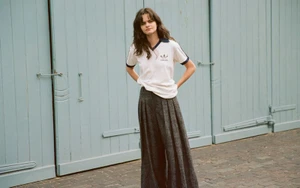 Model Ster Vieira wearing a white adidas polo shirt and wide dark trousers standing against light blue double doors