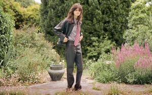Model Ster Vieira in black leather jacket and trousers standing in a lush garden for The Gentlewoman project Here.