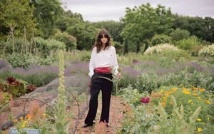 Model standing in a lush garden wearing a white collared shirt and dark trousers for The Gentlewoman editorial project