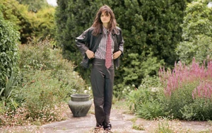 Model standing outdoors in a garden wearing a black leather jacket, striped shirt, patterned tie, and dark leather trousers.