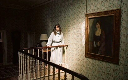Model Ster Vieira posing on a wooden staircase with patterned wallpaper and a framed portrait for The Gentlewoman.