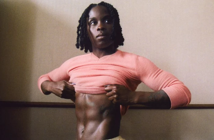 Black woman with braided hair wearing a pink sweater lifting it to show abs for AnOther Magazine Forces of Nature project
