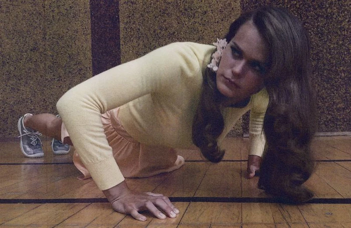 Woman in a yellow long-sleeve top and peach skirt doing push-ups on a wooden gym floor for AnOther Magazine