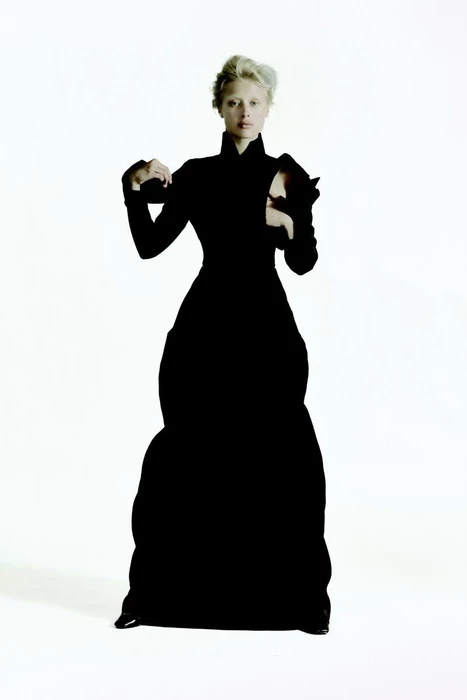 Model Ksenia Lifanova in a structured black gown standing against a bright white background for Vogue Portugal.