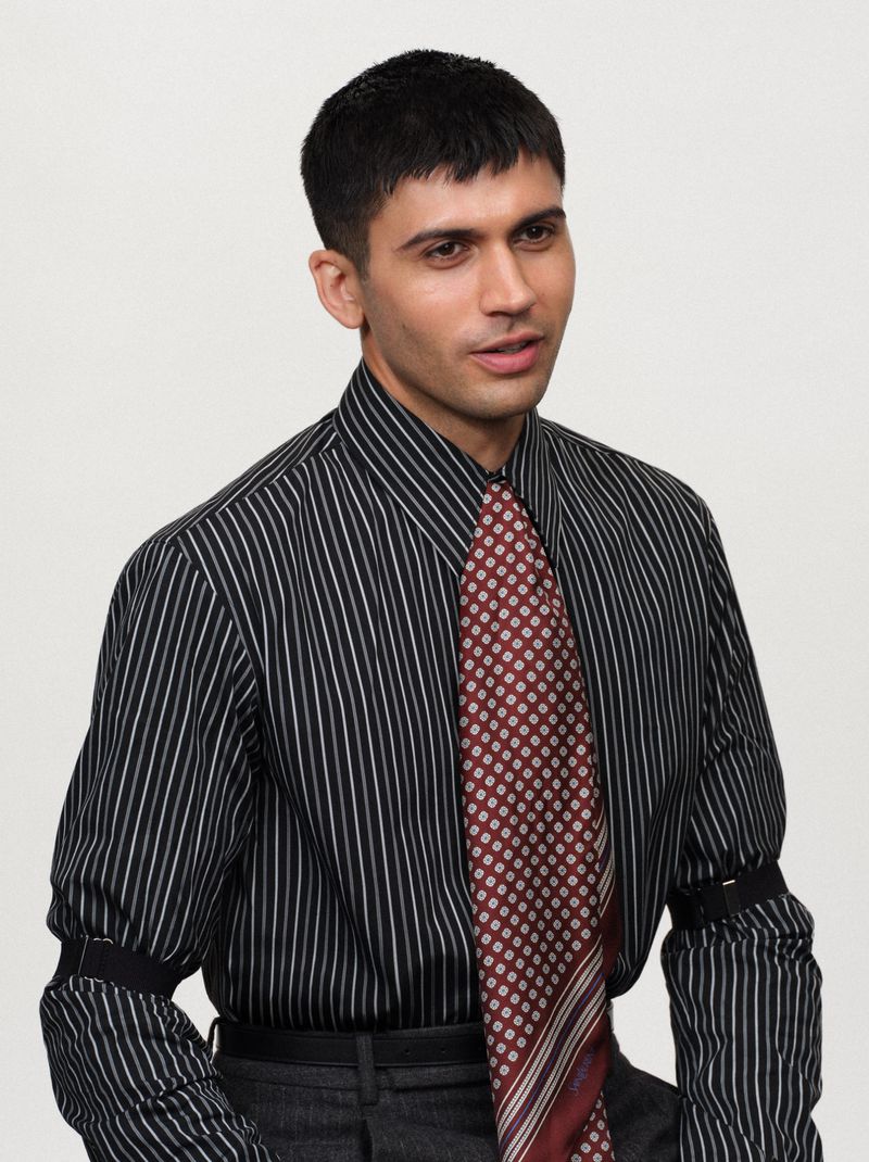 Man wearing a striped black shirt and patterned red tie against a plain light background