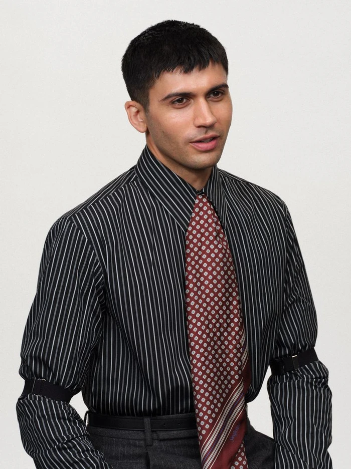 Man wearing a striped black shirt and patterned red tie against a plain light background