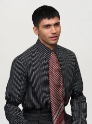 Man wearing a striped black shirt and patterned red tie against a plain light background
