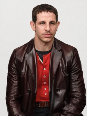 Man wearing a brown leather blazer and red buttoned top against a white studio background