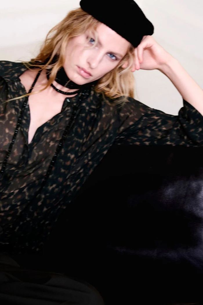 Model wearing a dark printed blouse and black beret resting her head against a dark surface for COS Pre-Winter 2026.