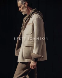 Richard Biedul wearing a cream wool jacket and brown hoodie against a dark background for Brett Johnson.