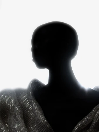 Silhouette of a bald Black woman wearing a sequined top against a stark white background in a minimalist fashion portrait.