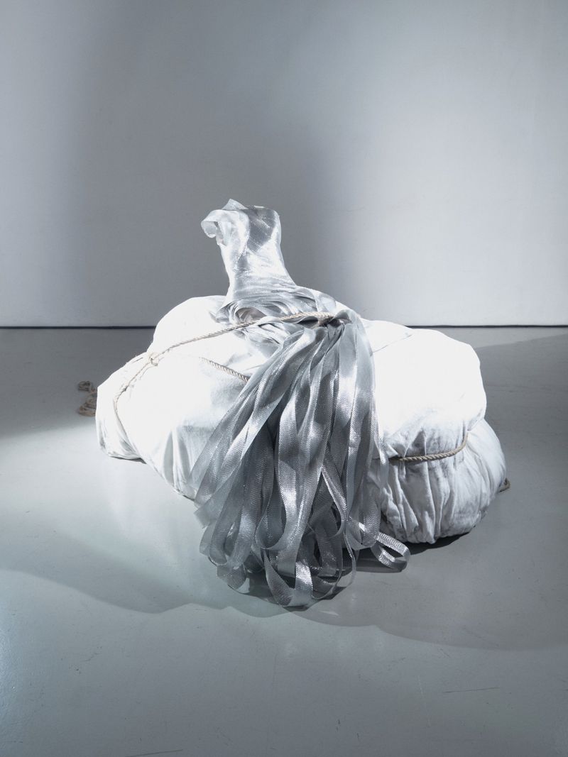 Abstract photograph of a wrapped white bundle with silver ribbon on a gray studio floor, capturing a contemporary fine art aesthetic.
