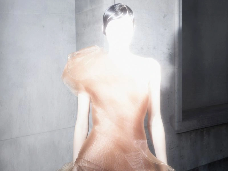 Silhouette of a model standing in a voluminous sculptural couture gown backlit by a bright rectangular doorway.
