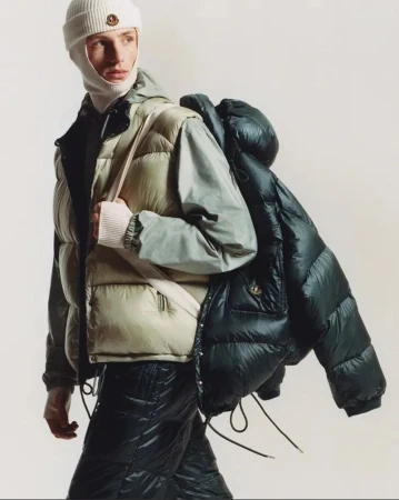 Model wearing a puffer vest, balaclava beanie, and backpack against a plain background for Moncler Re/Icons 2026
