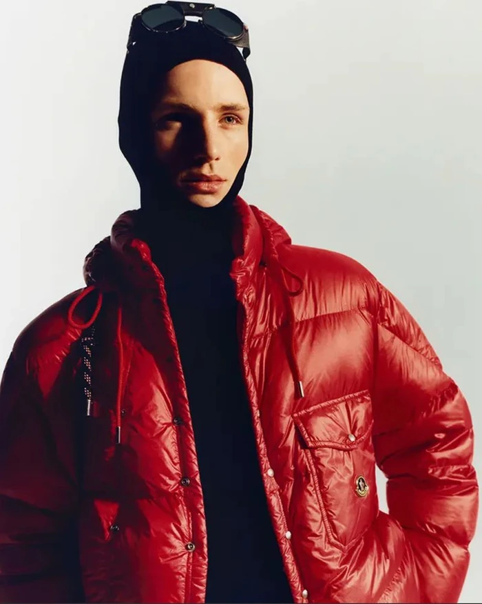 Model wearing a red puffer jacket and black balaclava with sunglasses on top against a white background