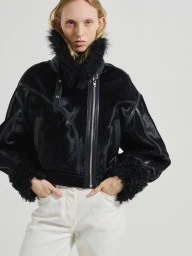 Model wearing a black fur-trimmed jacket with white trousers against a neutral background for Vaillant lookbook