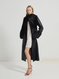 Model wearing a black leather coat with furry panels over a white patterned dress and red heeled sandals in a studio.