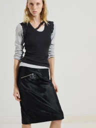 Model in grey and black layered top with black midi skirt against a plain white studio background.