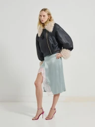 Model wearing a black leather jacket with faux fur trim and a light blue satin skirt against a white studio background.