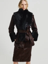 Model wearing a patterned brown belted coat with black fur collar and cuffs against a plain grey studio background