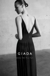 Model in a black pleated dress with a low V-back and delicate pendant necklace against a textured wall