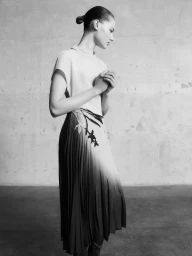 Model Famke van Hasselt wearing a patterned pleated skirt in a monochrome editorial portrait for Giada FW26