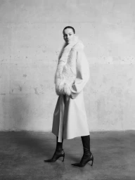 Model Famke van Hasselt wearing a belted coat with a fur stole and black boots against a concrete wall