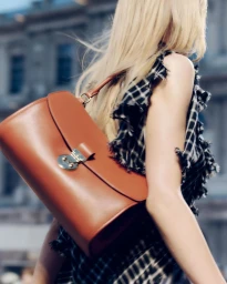 Blonde model carrying a brown leather shoulder bag wearing a black and white plaid dress outdoors