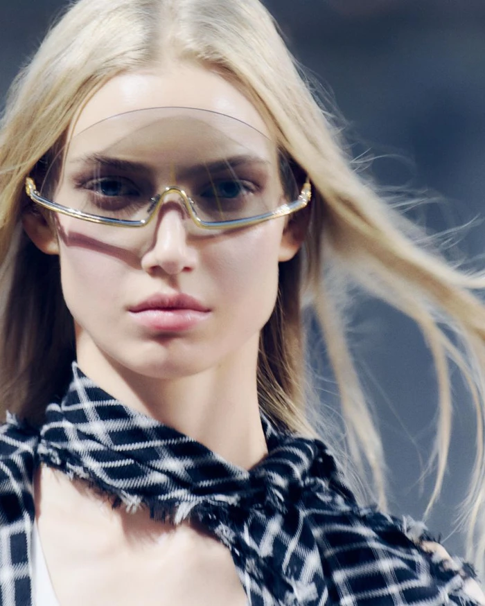 Close-up of a female model wearing futuristic wrap-around sunglasses and a black and white patterned scarf.
