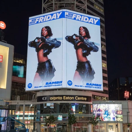 Billboard at night features a model promoting Bambii's 'New EP-Infinity Club II' on Spotify against a modern building backdrop in Toronto.