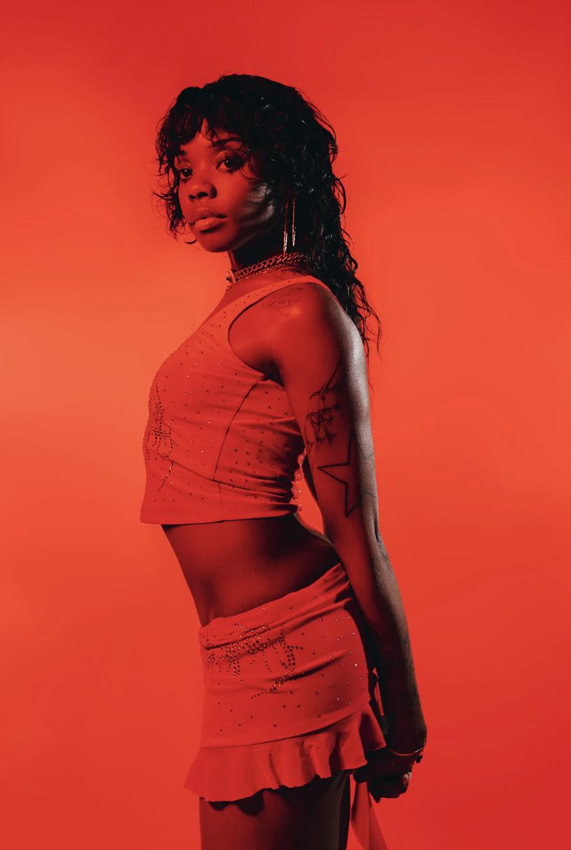 Young Black woman in a coral-colored outfit poses against a matching coral background, showcasing a Y2K aesthetic.