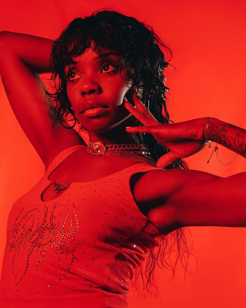 Portrait of a young African-American woman with hand near her face posing in front of a vibrant red backdrop with chain necklace.