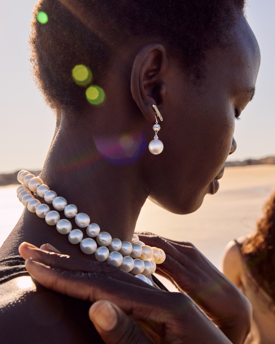 Close-up of an African-American woman wearing pearl earrings and necklace outside, possibly for a fashion or beauty campaign.