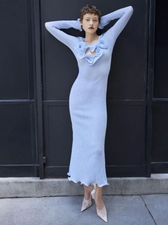 Model Daria Zolotova in a long light blue knit dress posing with arms raised against a dark paneled wall.