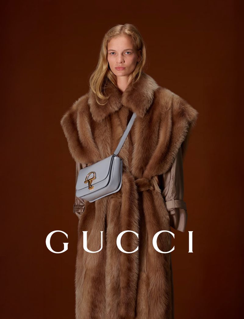 Fashion shot of a woman wearing a fur coat and a light blue purse, set against a warm brown backdrop with the brand name Gucci.