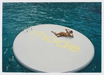 Hailey Bieber lounging on a large round float with the rhode branding in the middle of blue water