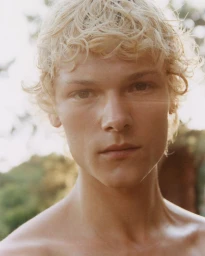 Close-up portrait of a young man with curly blonde hair outdoors in natural sunlight for Coperni