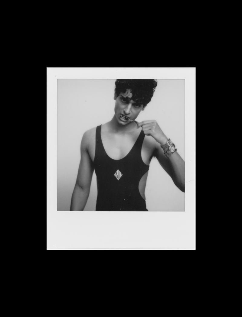 Black and white portrait of a person in a leotard holding a toothbrush, framed by a white Polaroid border on a black background.